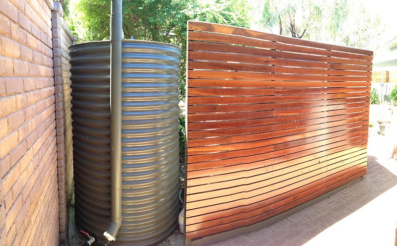 slimline rainwater tank oval shape with wooden fence to hide it