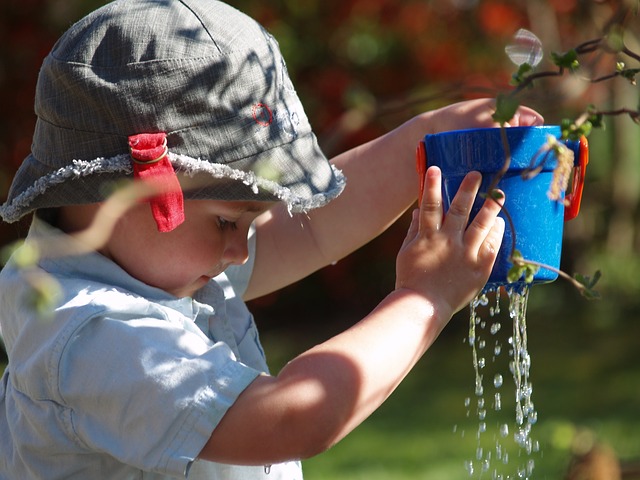 Child holding a water can with holes and water dripping through